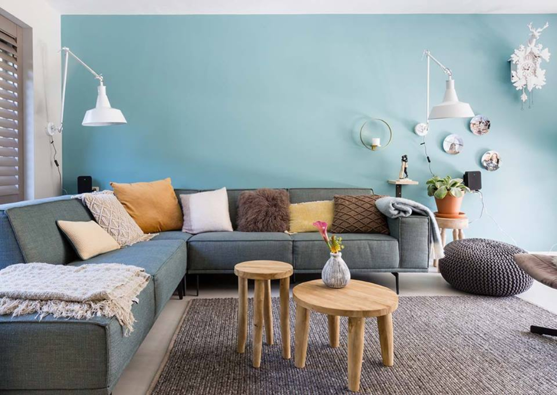 Woonkamer met een beton ciré vloer. Gestyled met meubels, kussentjes en een lichtblauwe wand.