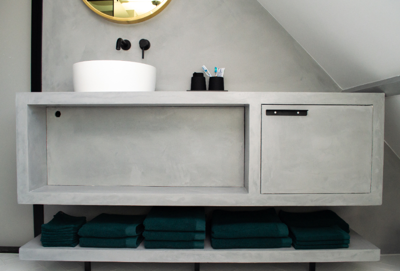 Lichtgrijs beton ciré badkamer meubel met groene handdoeken en zwarte accessoires